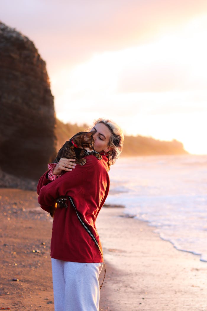 A woman lovingly holds her cat by a coastal cliff at sunset, showcasing serene companionship.